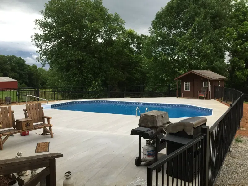 A large swimming pool is surrounded by a fence and a grill.