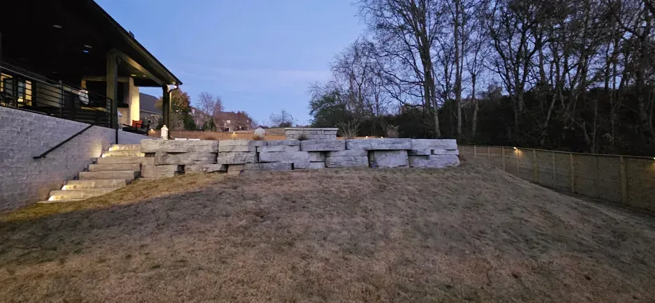 A large stone wall with stairs leading up to it is in the backyard of a house.