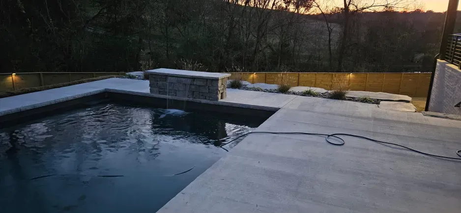 A large swimming pool is surrounded by trees and a concrete patio.