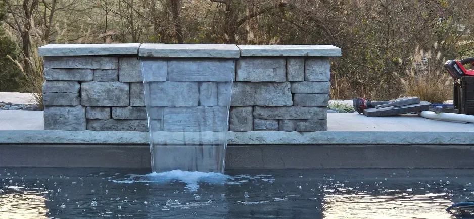 A waterfall is coming out of a stone wall into a pool.