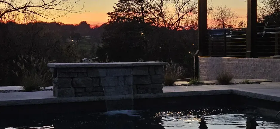 A sunset over a swimming pool with a fountain in the middle