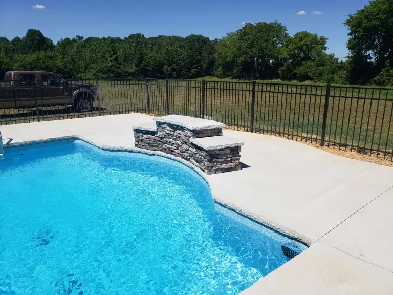A swimming pool with a fence around it and a truck parked in the background.