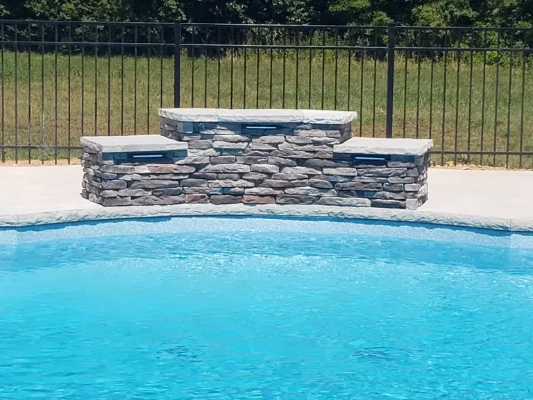 A swimming pool with a stone wall and a fence in the background.