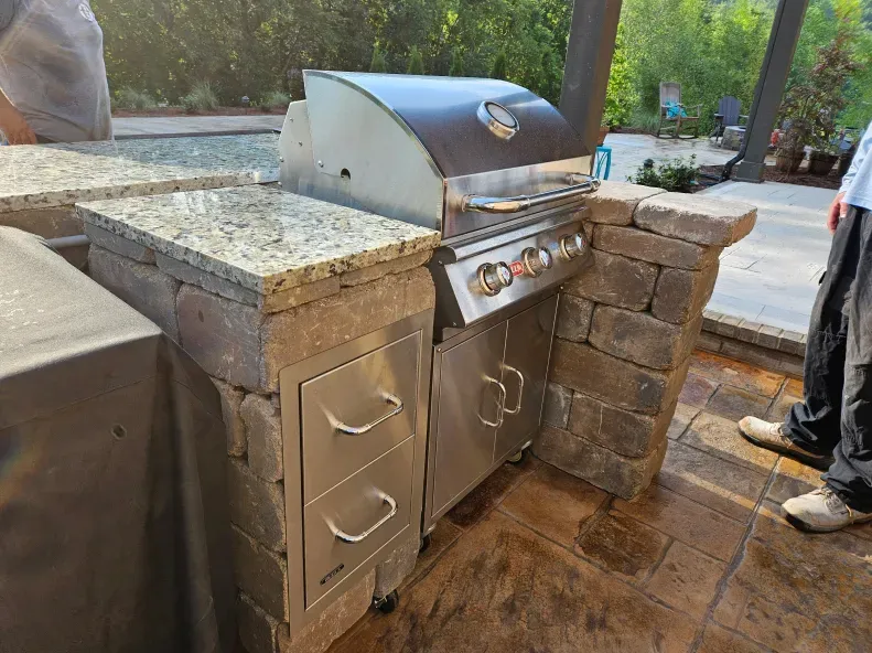 A man is standing next to a grill in an outdoor kitchen.