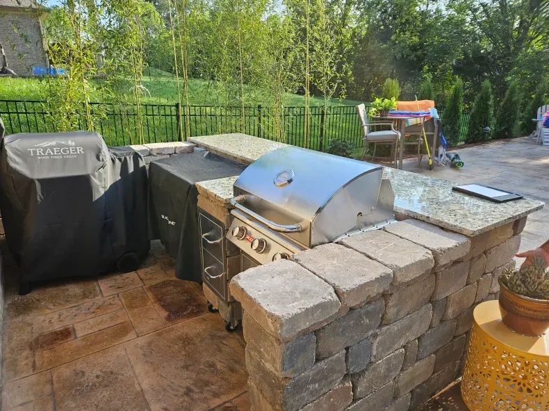 A grill is sitting on top of a brick counter in a backyard.