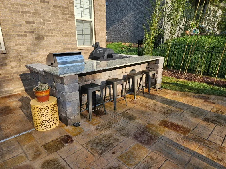 A patio with a grill and stools in front of a brick house.