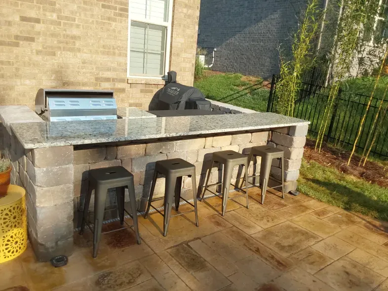 A patio with a grill and stools in front of a brick house.