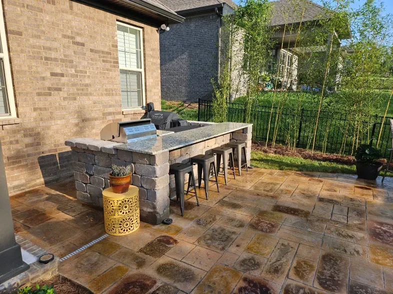 A patio with a grill and stools in front of a brick house.