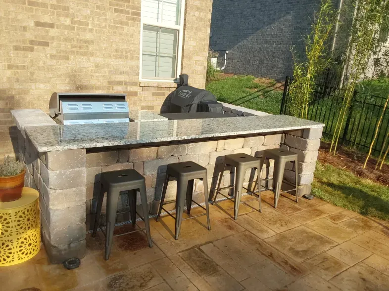 A patio with a grill and stools in front of a brick house.