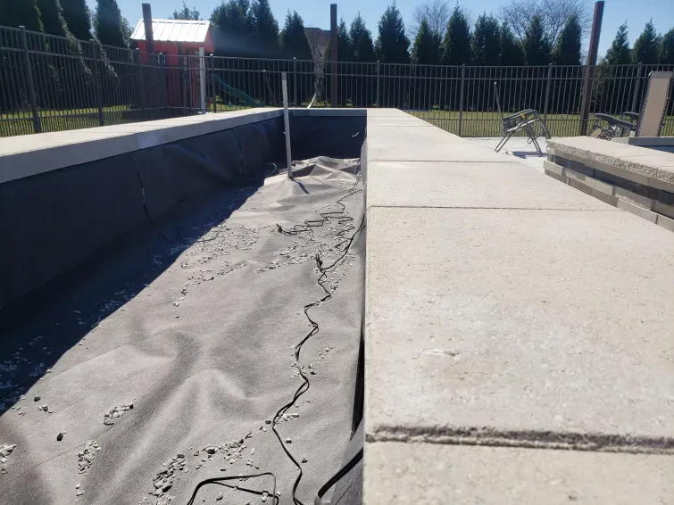 A concrete walkway leading to a swimming pool with a fence in the background