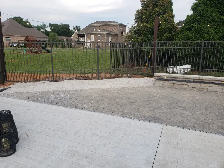 A fence is surrounding a concrete area with a house in the background