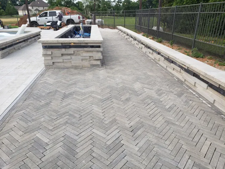 A brick walkway leading to a pool with a fence in the background.