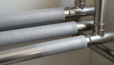 Three silver insulated pipes connected to shiny metal plumbing in a utility space