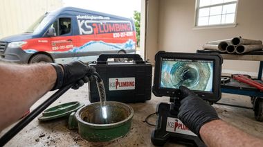 Plumber inspecting a sink drain with a borescope in a workshop garage, van visible outside.