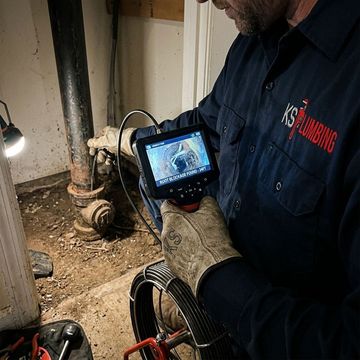 Plumber inspecting a pipe leak with a handheld camera in a basement crawlspace