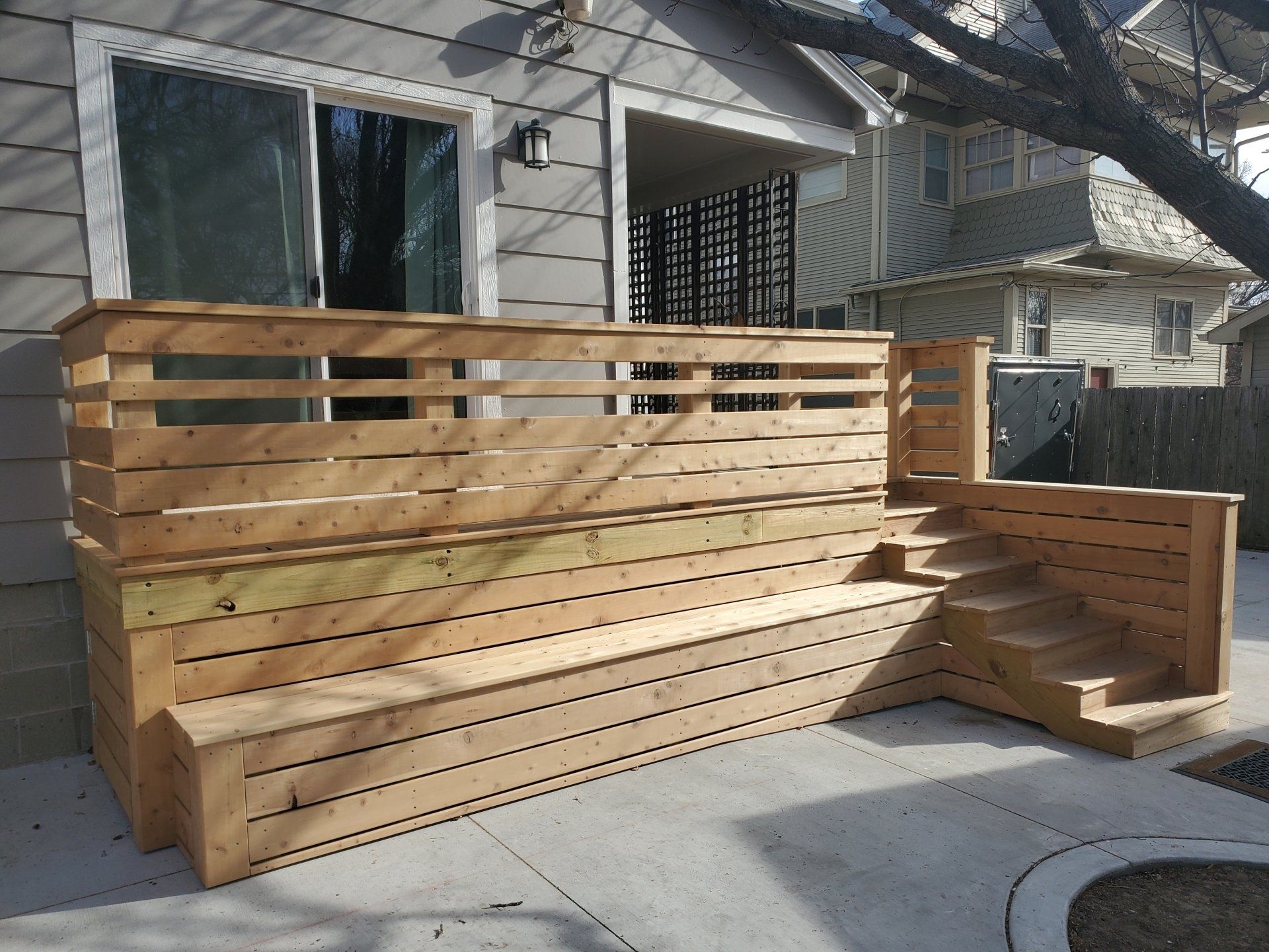 Wooden deck with stairs, built against a house with a sliding glass door.