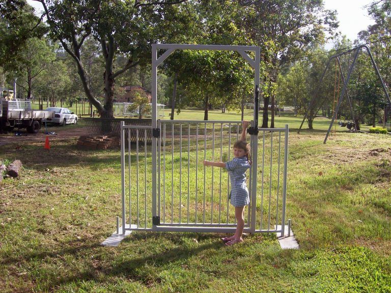 A little girl is standing in front of a metal gate
