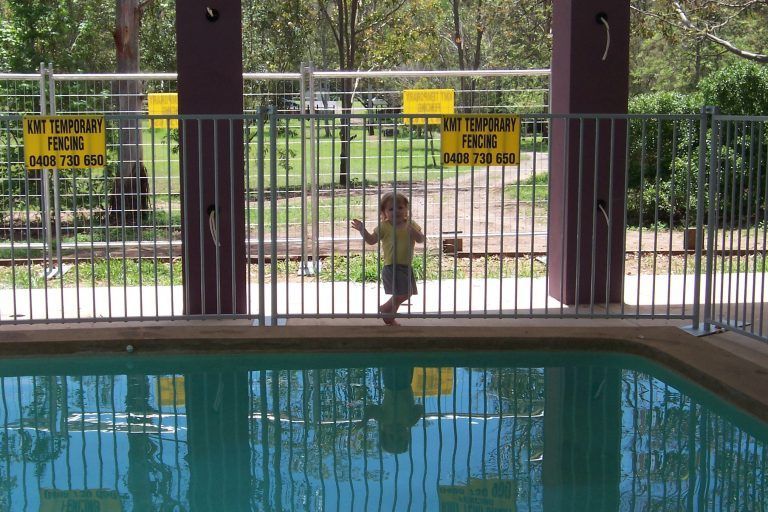 A little girl stands in front of a pool with a sign that says