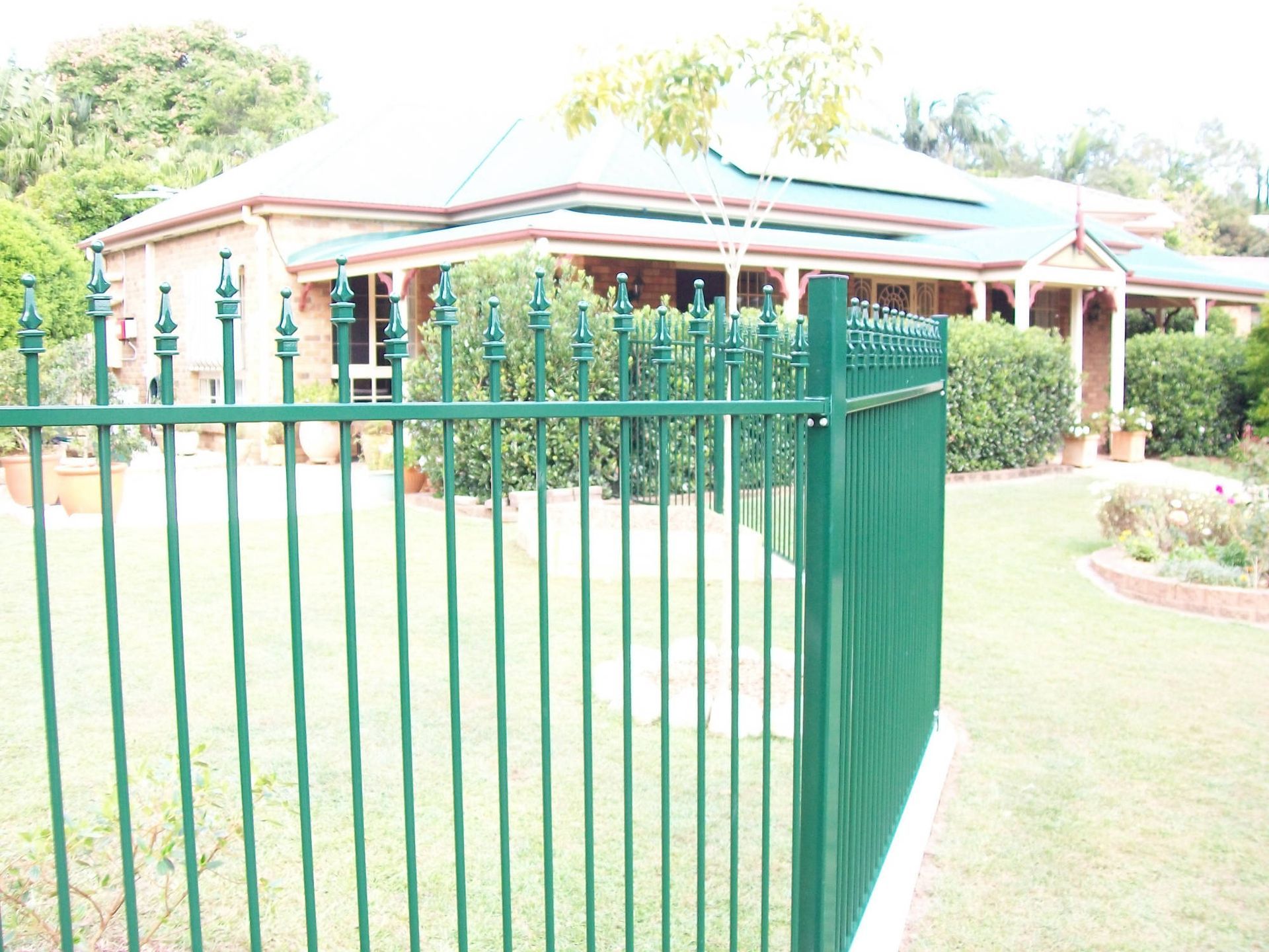 A green fence with a house in the background