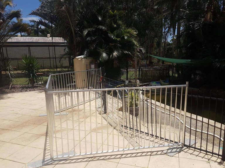 A stainless steel fence surrounds a patio next to a pond.