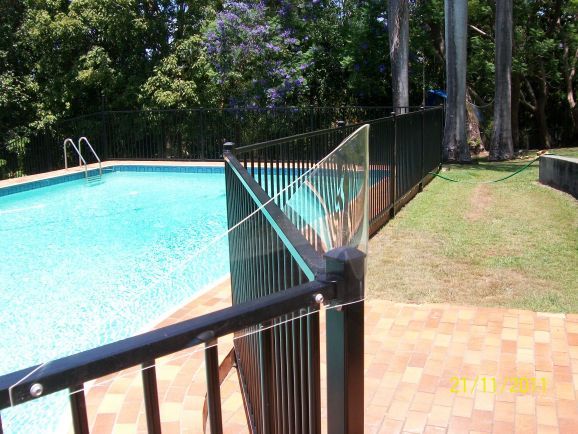 A black fence surrounds a swimming pool with trees in the background