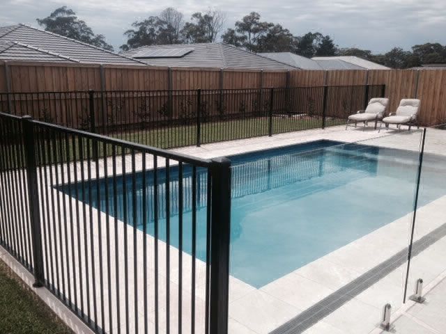 A fence surrounds a large swimming pool in a backyard.