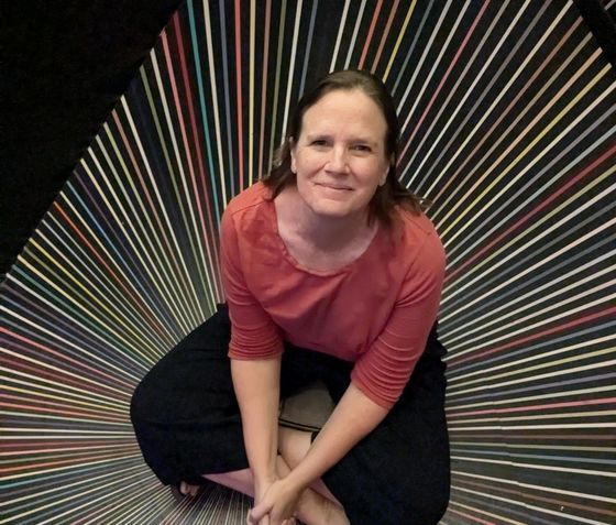 A woman in a red shirt is sitting in front of a colorful striped wall