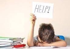 A young boy is sitting at a desk holding a sign that says `` help ''. Executive Functioning Coaching.