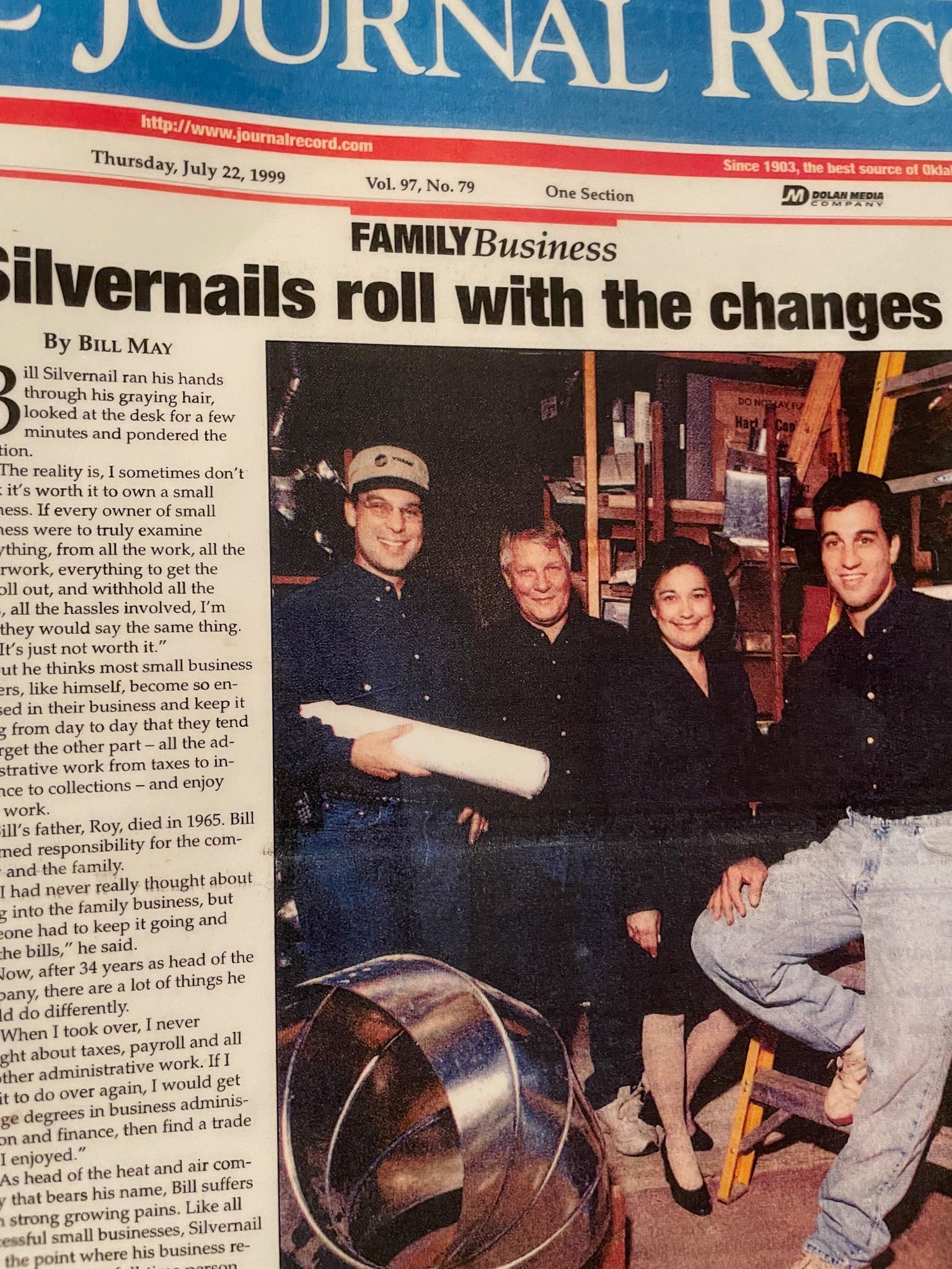 Family poses for newspaper article. Three men, one woman, inside a work setting with tools.