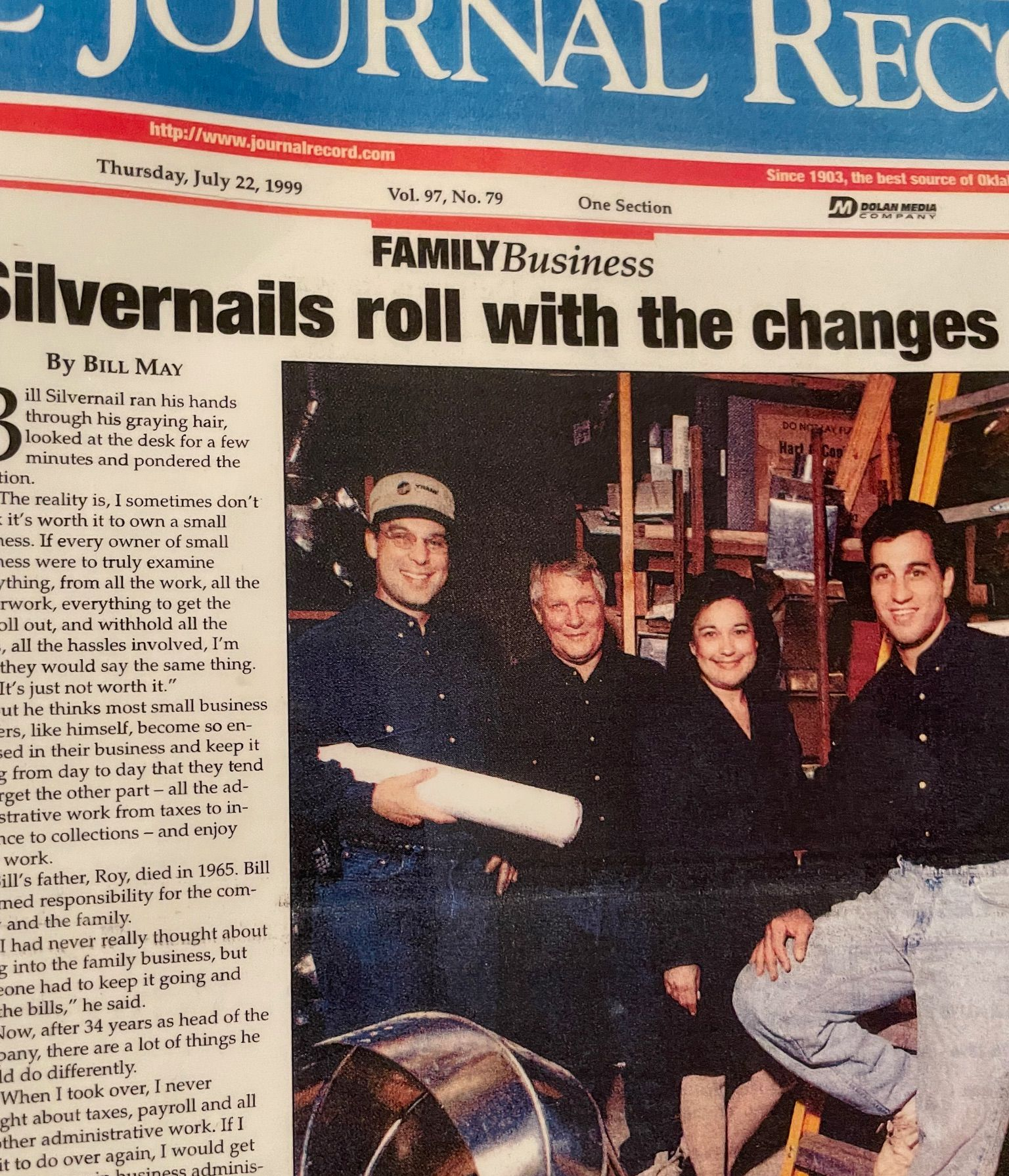 Family poses for newspaper article. Three men, one woman, inside a work setting with tools.