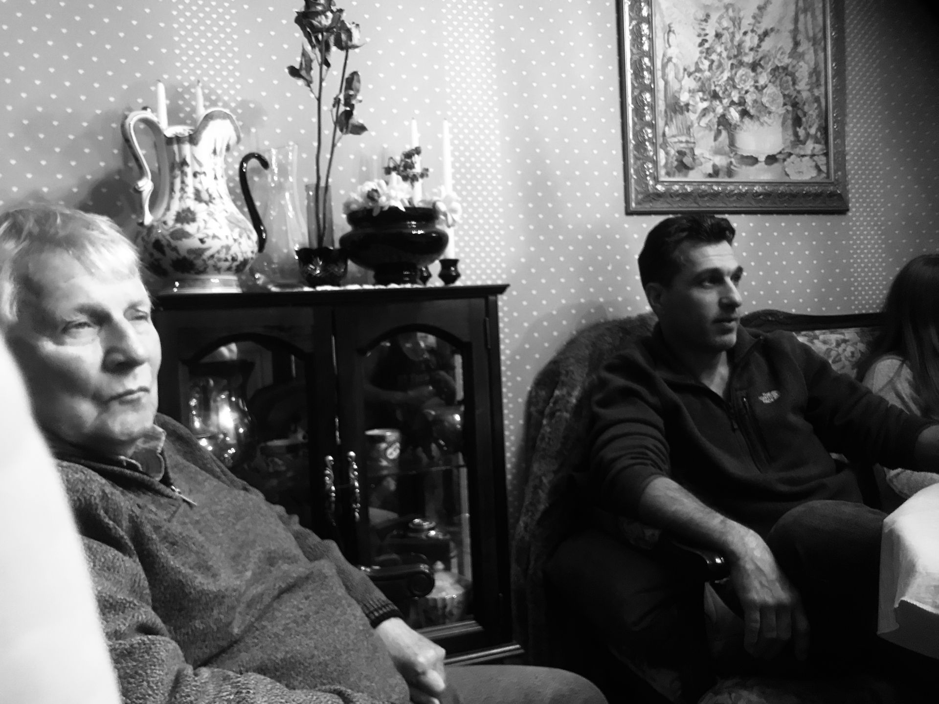 Older woman and man in a living room, possibly family. Antique decor and furniture. Black and white photo.