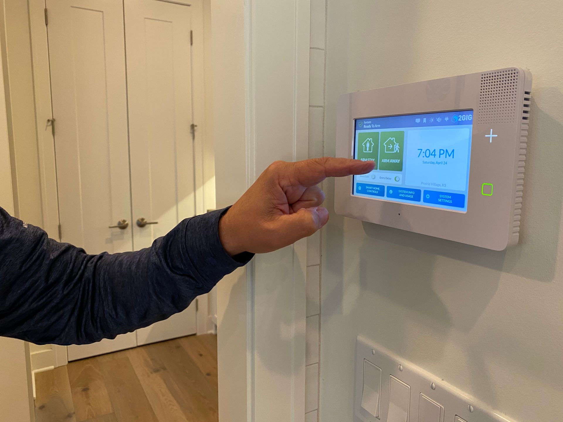 Person's hand touching a smart home control panel on a white wall. Panel shows temperature and settings.