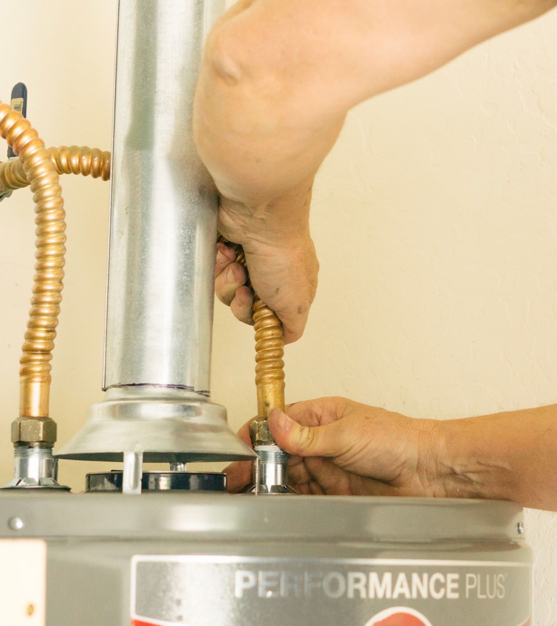 Person connecting a copper pipe to a silver water heater, likely installing or repairing plumbing.