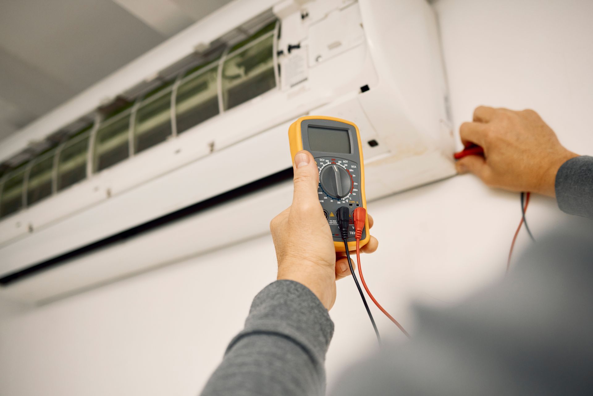Person testing an air conditioner with a multimeter.