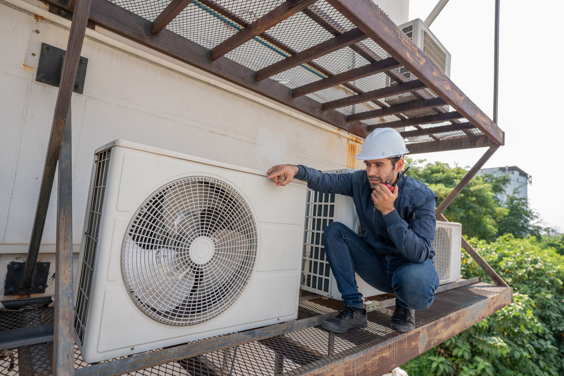 Man in hard hat inspecting an AC unit on a rooftop, pondering the issue.