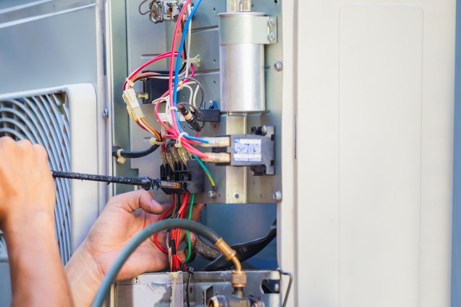 A technician repairs an outdoor air conditioning unit, working with wires and tools.