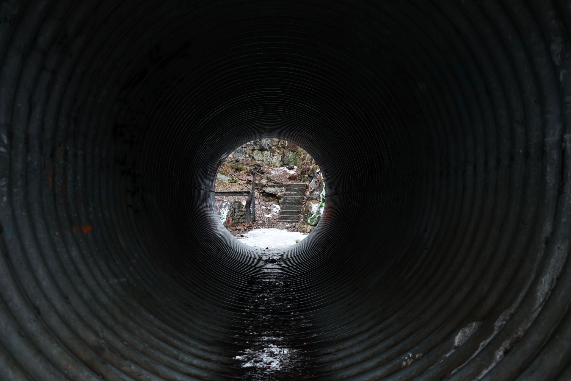 Inside a corrugated metal tunnel, looking out at a snowy outdoor scene.