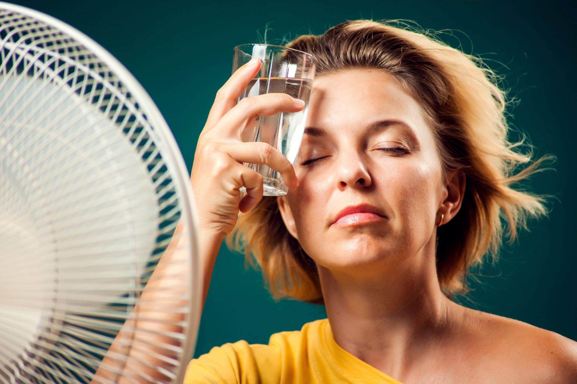 Woman in front of a fan holding a clear glass to head.