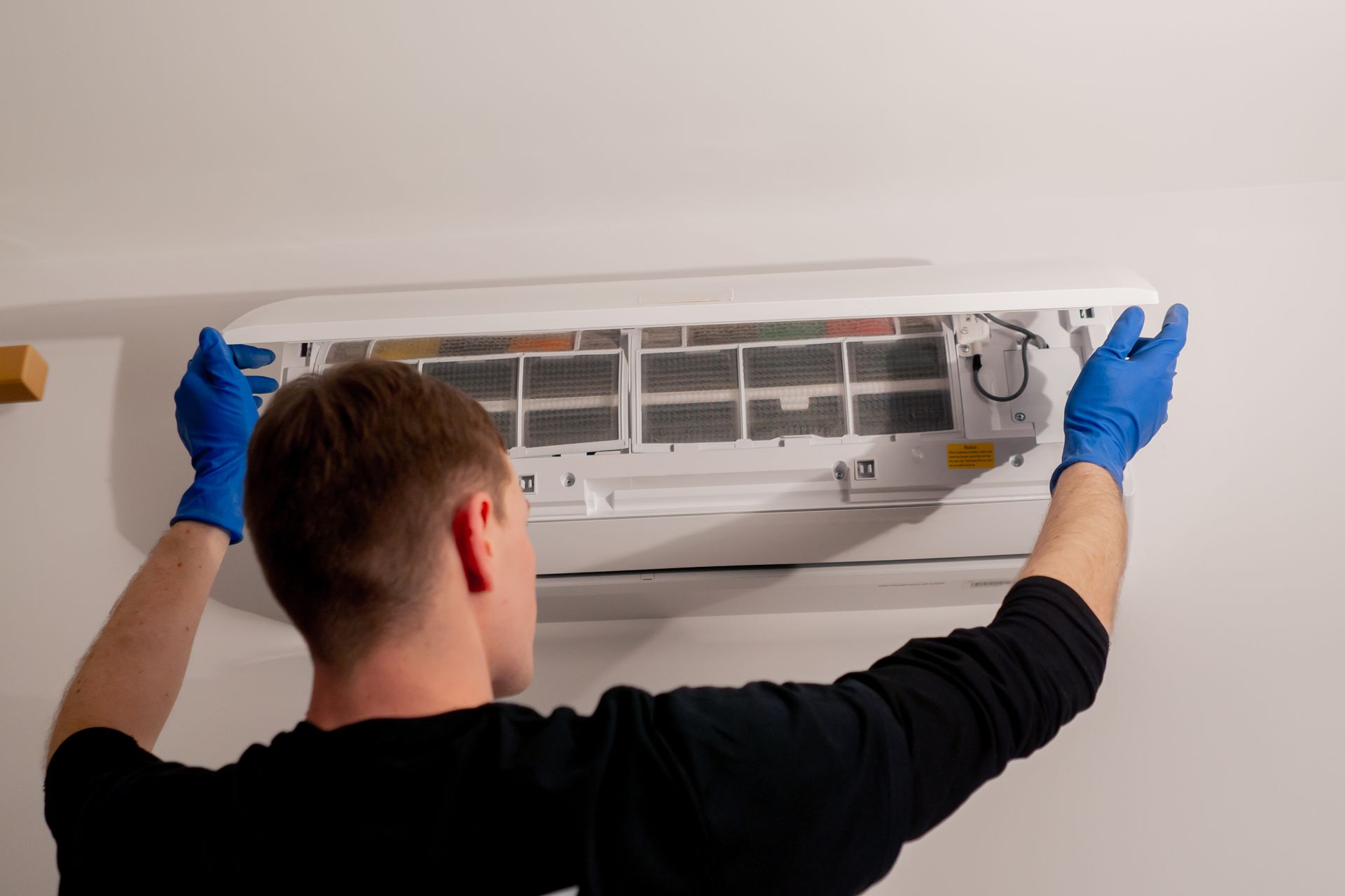 Person in blue gloves cleaning an air conditioner filter on a white wall.