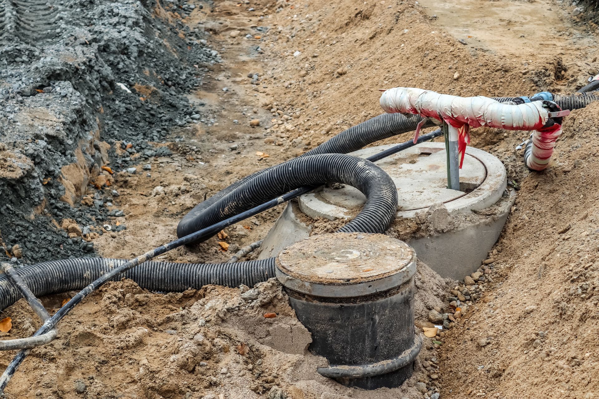 Two concrete septic tanks in sand, with black hoses and a red and white pipe connection.