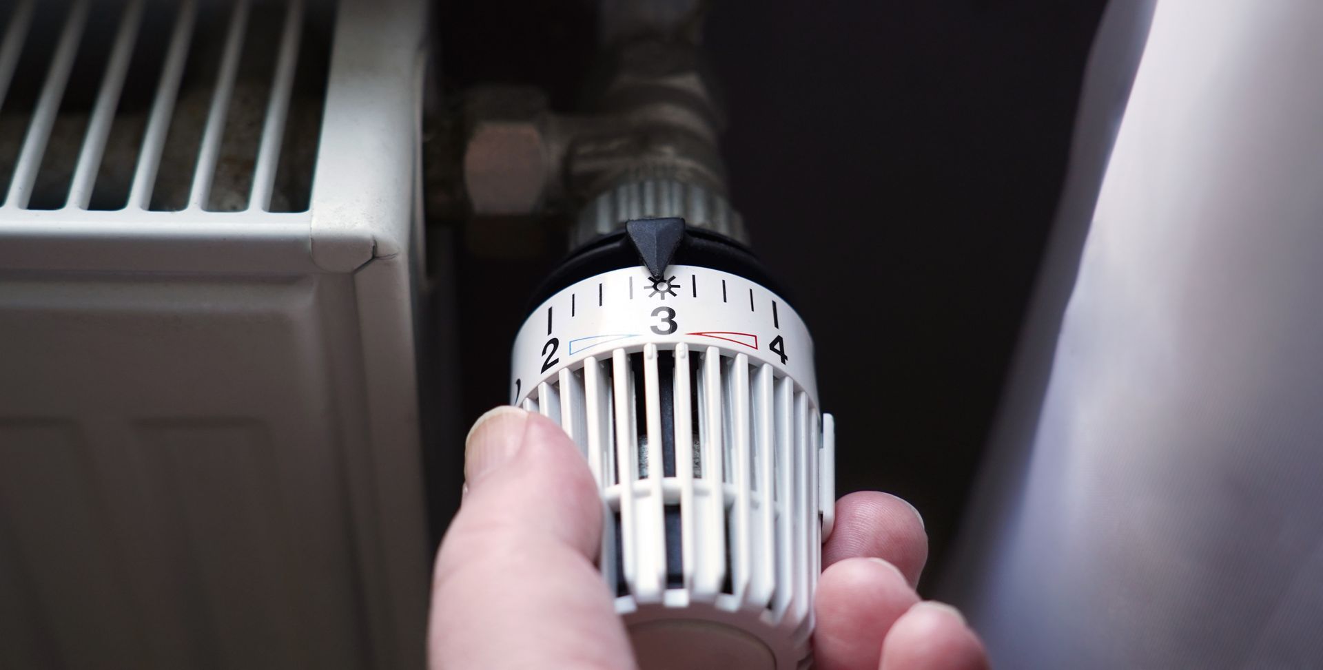 Hand turning a thermostat knob on a white radiator, setting it to level 3.
