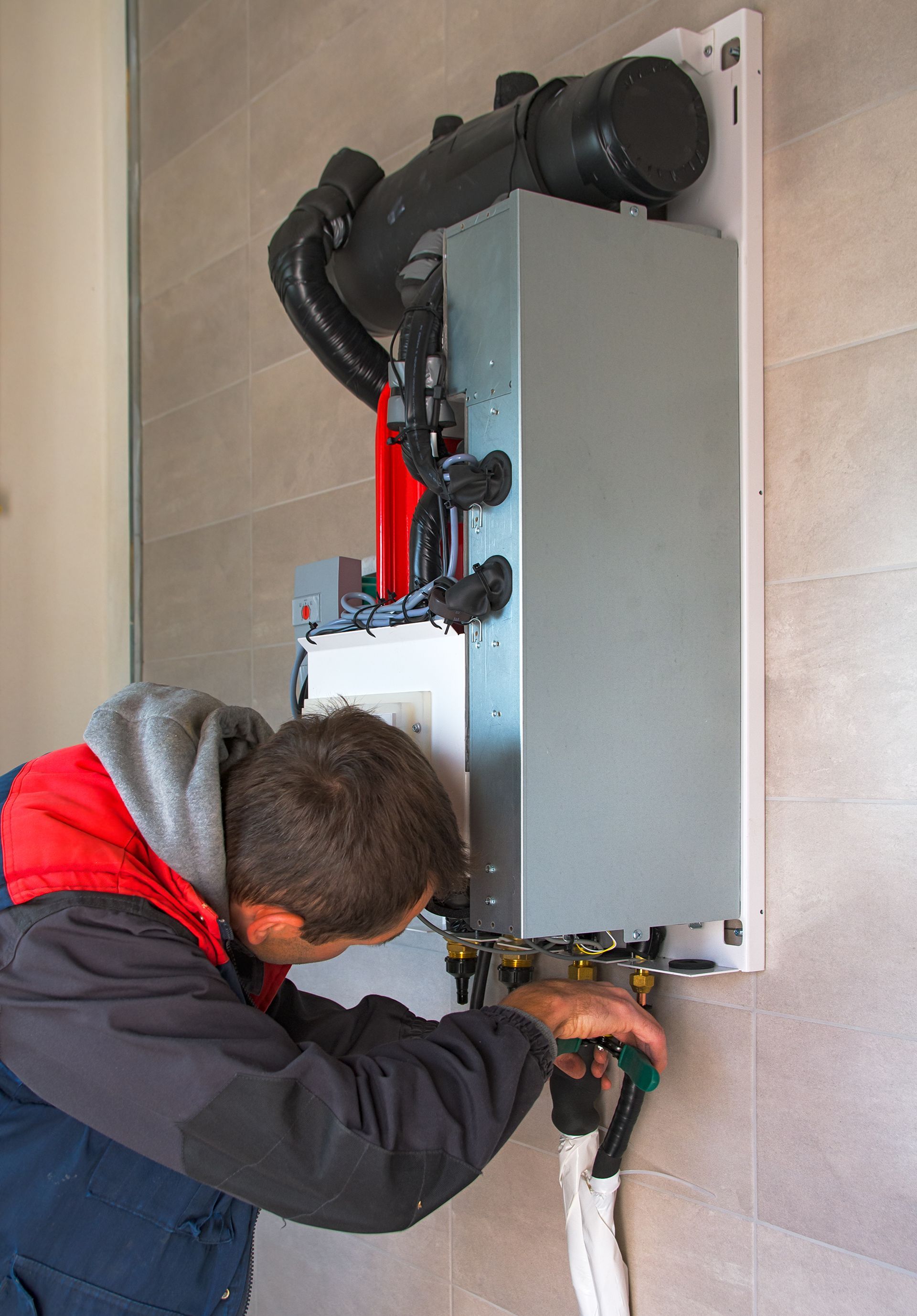 Man in work clothes installing or repairing a wall-mounted heating system.