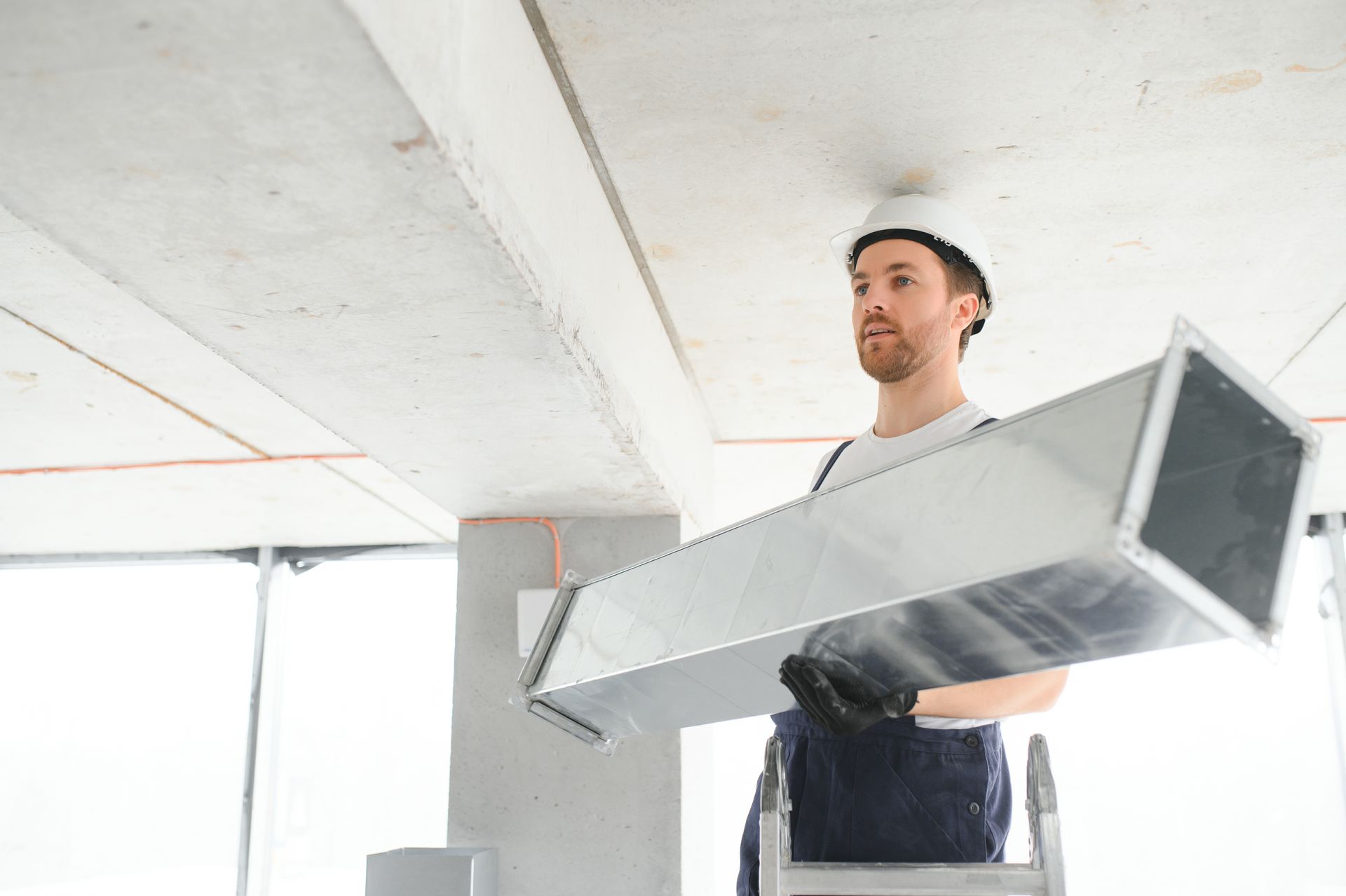 HVAC worker in a hardhat installing air duct in unfinished building.