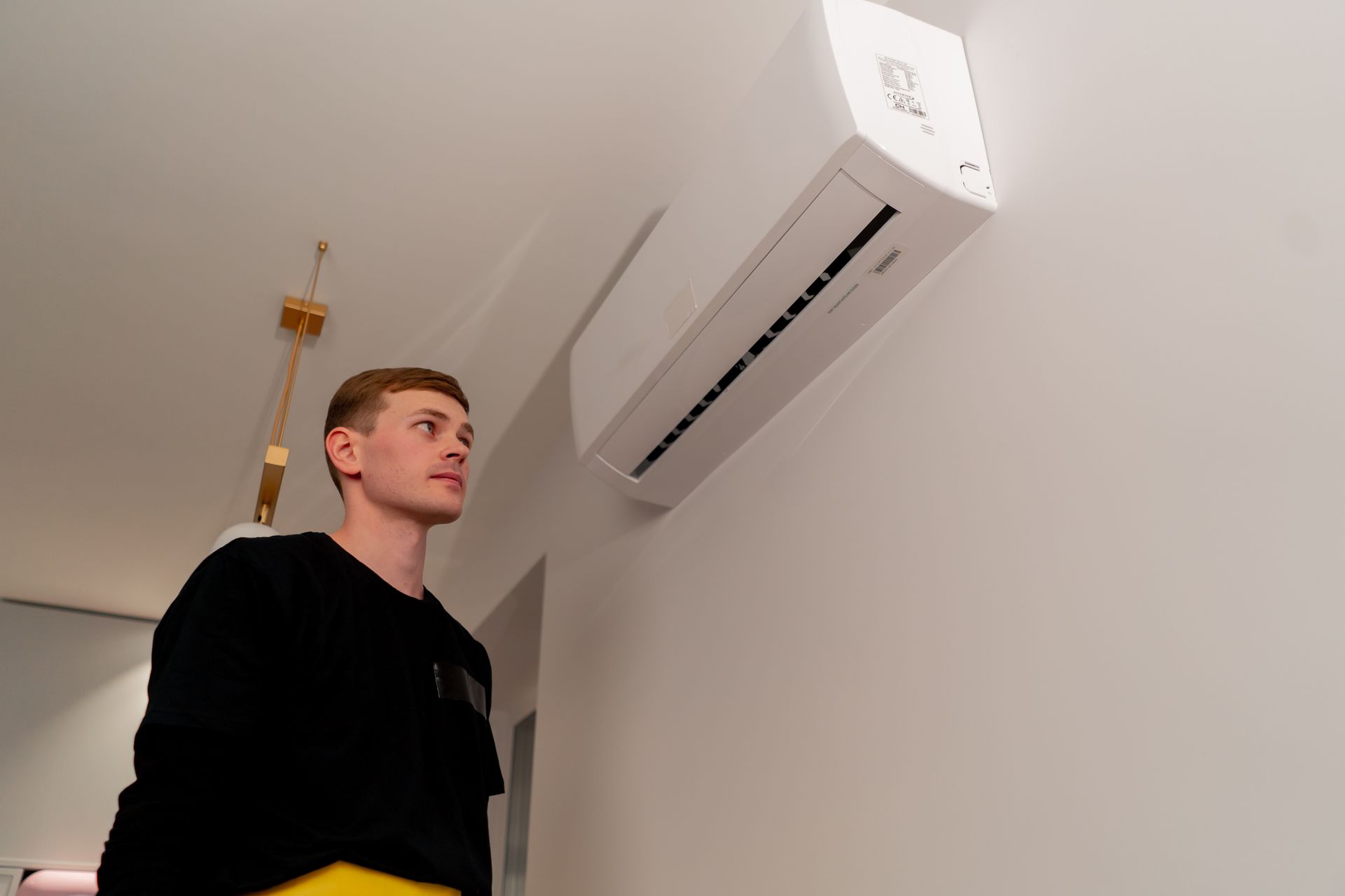 Man looking up at a white air conditioner mounted on a white wall.