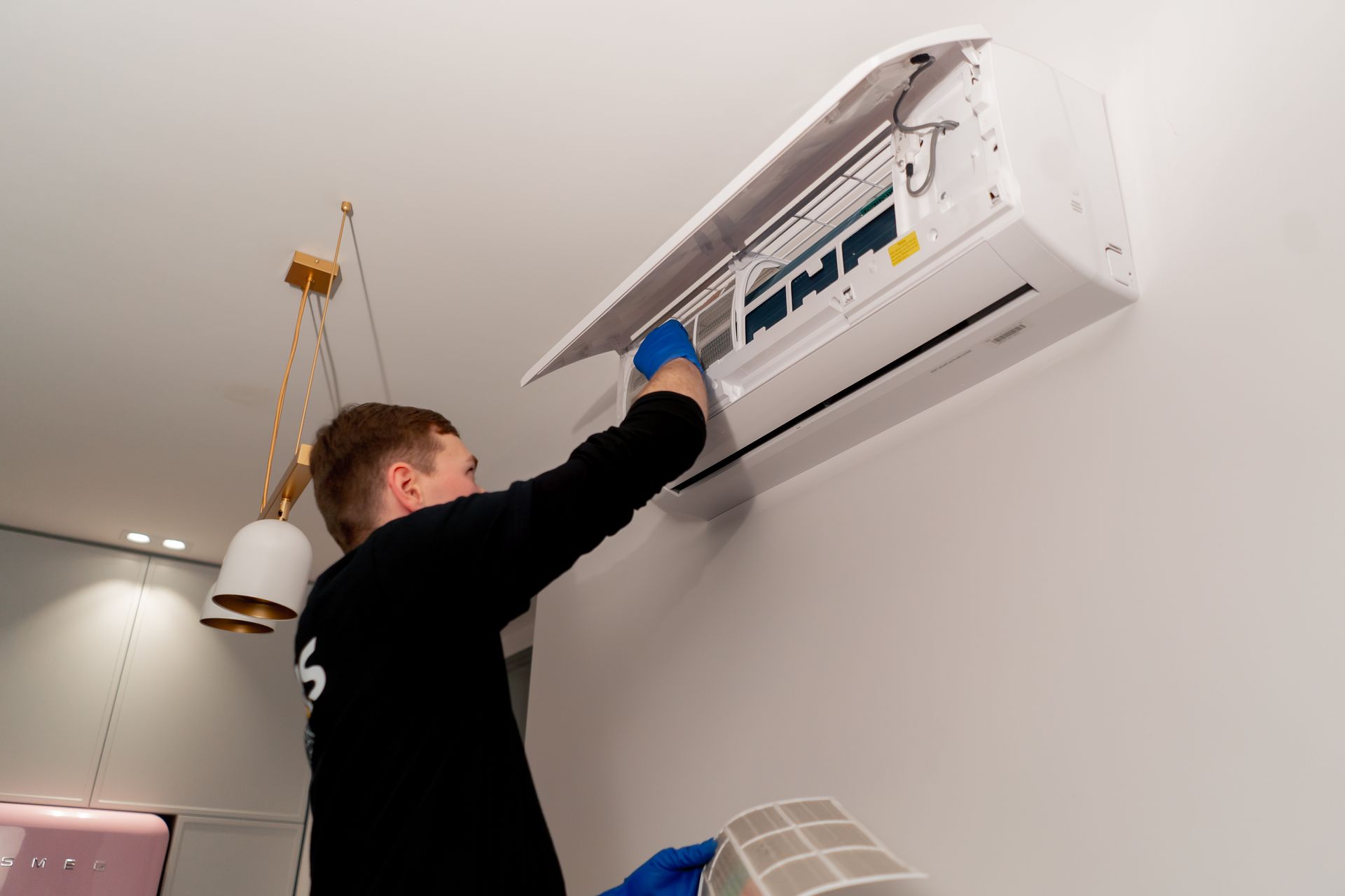 Man in blue gloves cleaning an air conditioner on a white wall.