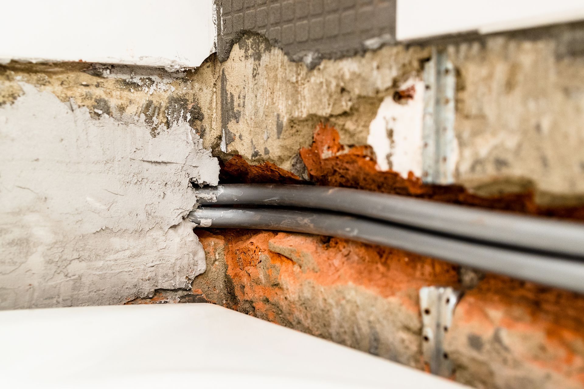 Electrical wires running through brick and plaster, with metal brackets.