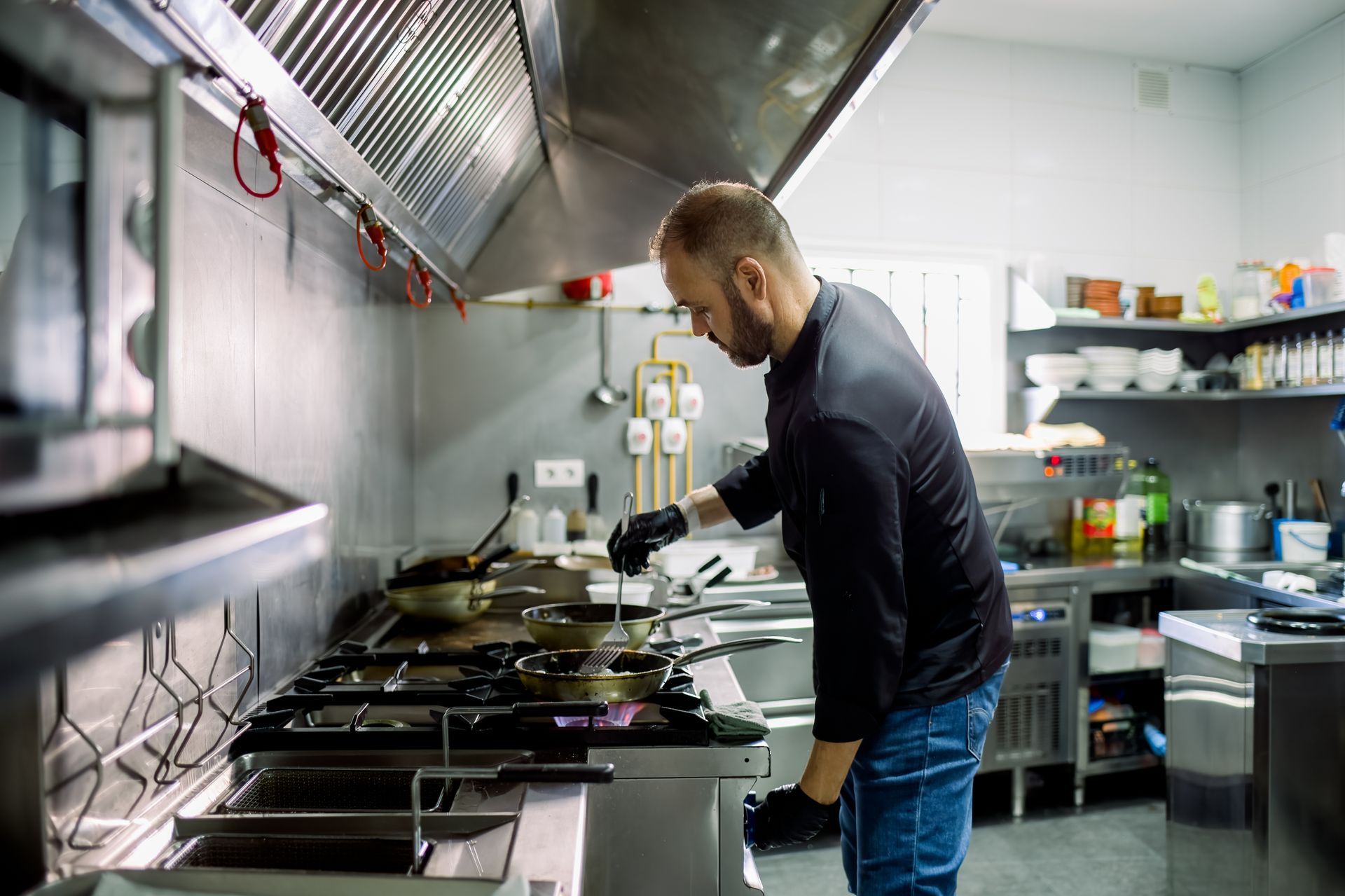 Chef in black gloves cooking on a gas stove in a commercial kitchen.
