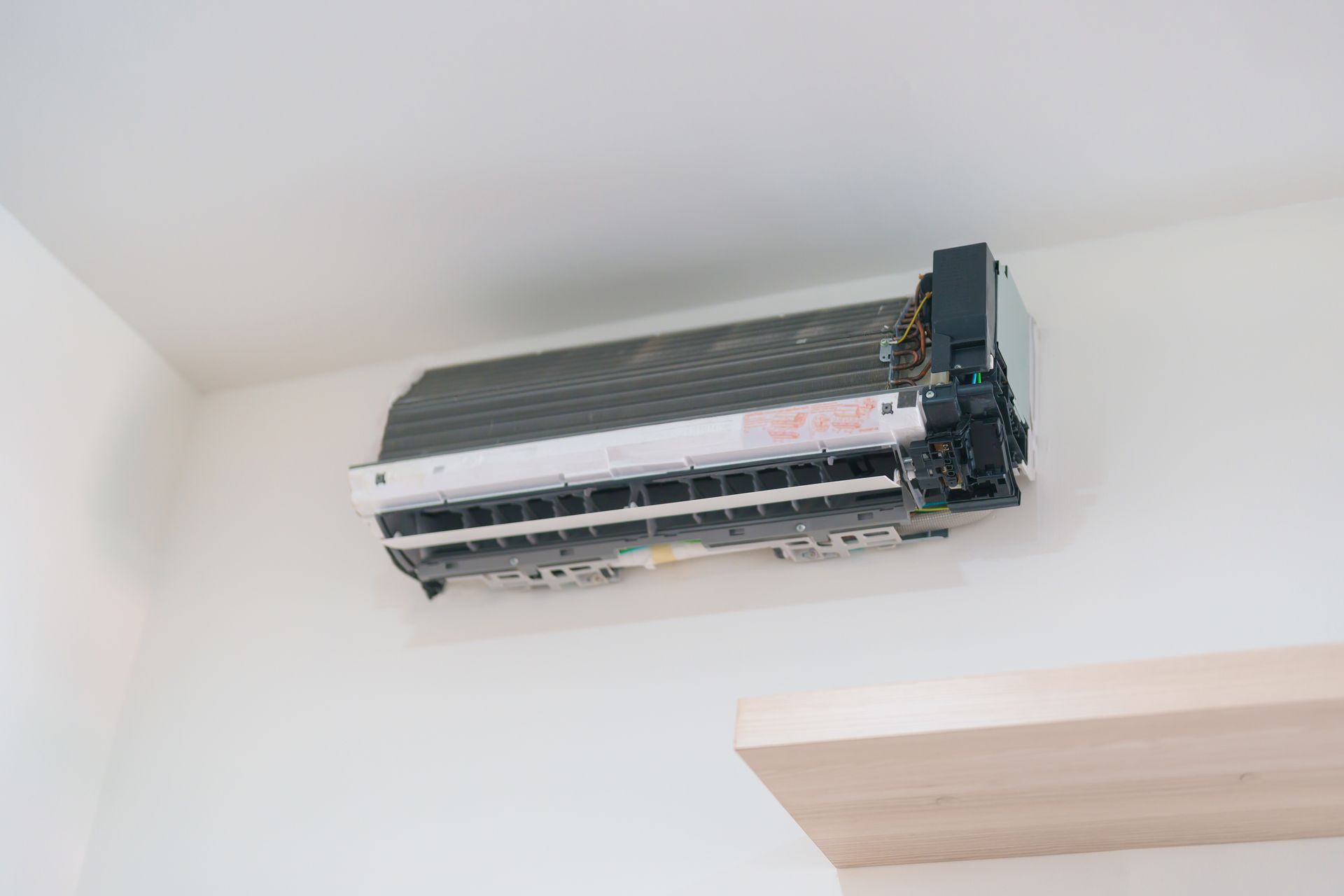 Dirty, wall-mounted air conditioner unit on a white wall, positioned above a wooden shelf.