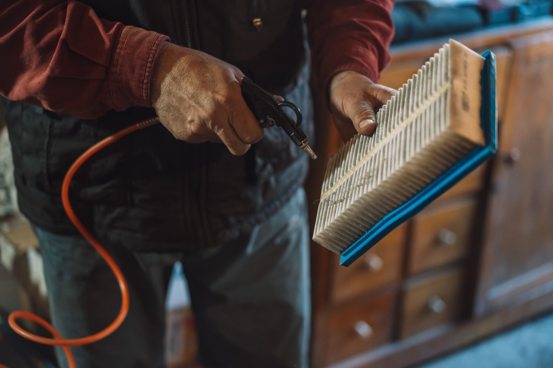 Person blowing air on a rectangular air filter with an air gun in a workshop.