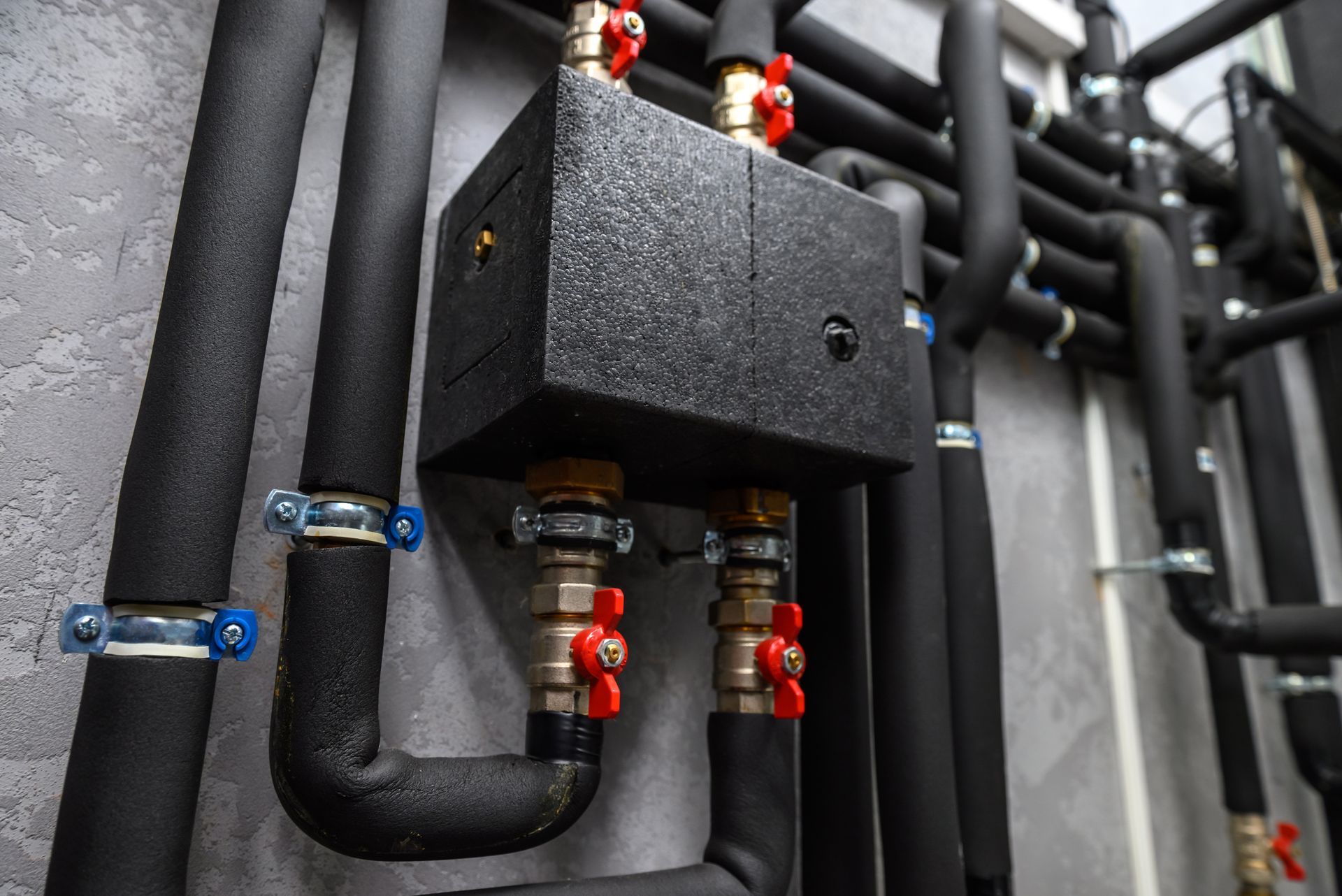 Pipes and valves, connected to a black box, secured against a gray wall.